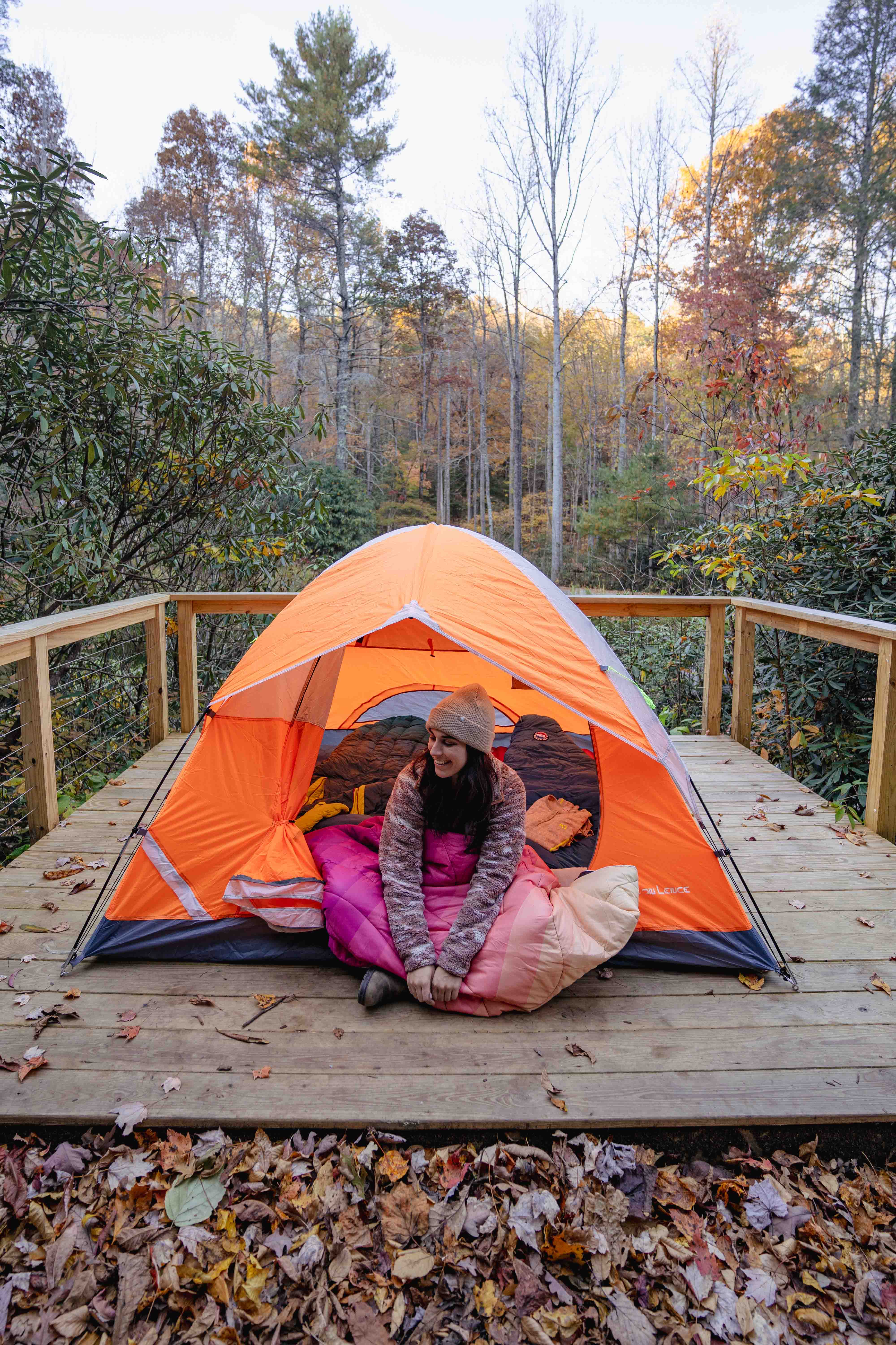 Woman sitting inside orange tent surrounded by trees