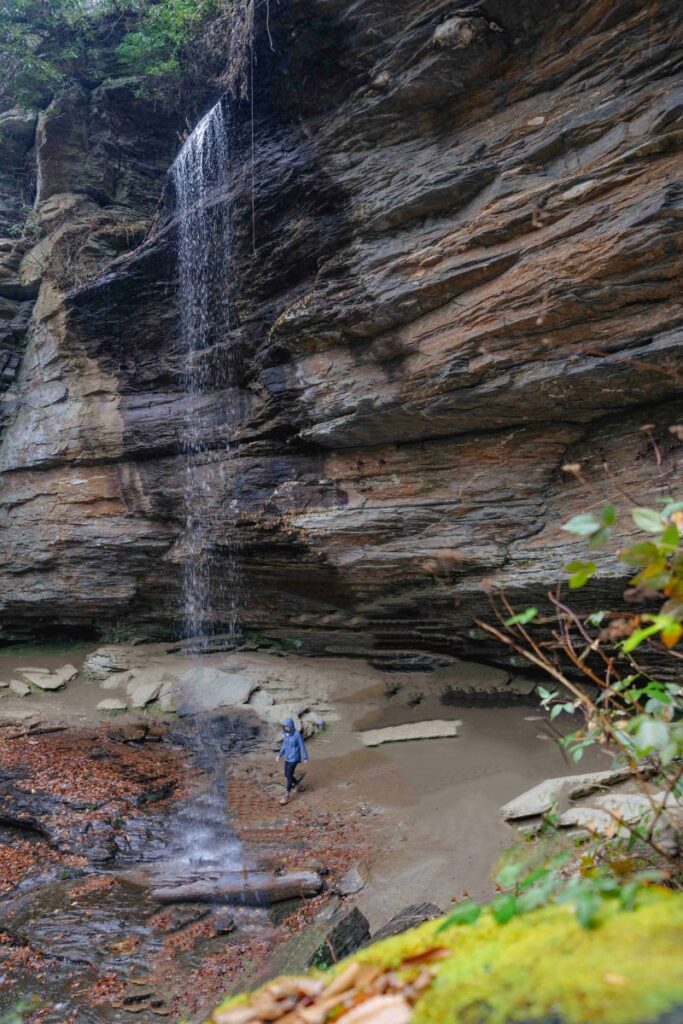 Woman in blue rain jacket standing behind Moore Cove Falls