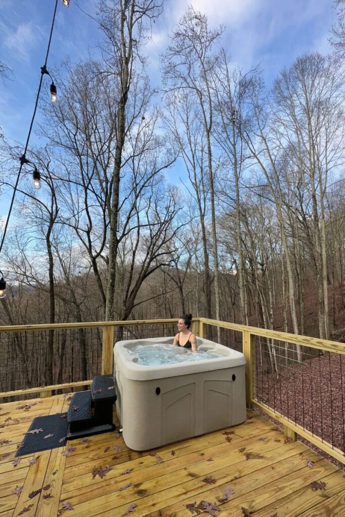 Woman sitting in a hot tub on a deck surrounded by trees
